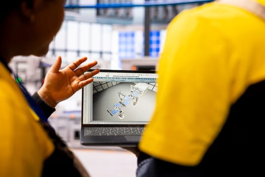 African american engineers use software for optimization of robotic arms and conveyor belts systems in autonomous factory. Automation and smart manufacturing revolutionize industrial plant production.