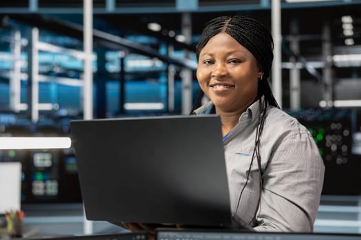 Portrait of smiling data center software developer using artificial intelligence neural networks. Cheerful server farm worker uses AI programming language on computer, configuring specialized hardware