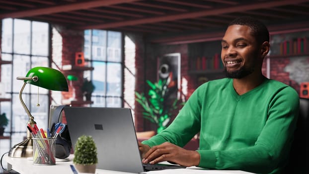 Black teleworker at home desk opening laptop to edit documents and solve daily tasks, updating reports and files. Young employee doing remote job and managing digital paperwork. Camera A.
