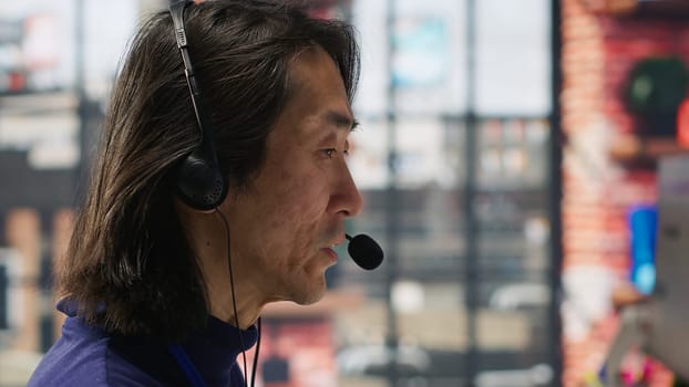Closeup of senior call center agent helping customers regain access to accounts, resetting passwords. Experienced Asian worker in diverse customer center assisting clients needing help, camera A