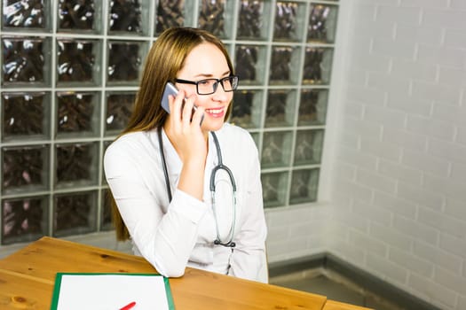 Portrait of young woman doctor in white coat using phone