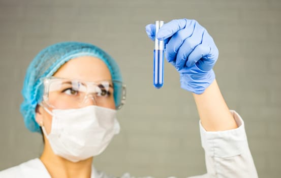 Close-up of glass tube with blue fluid in nurse hand during medical test.
