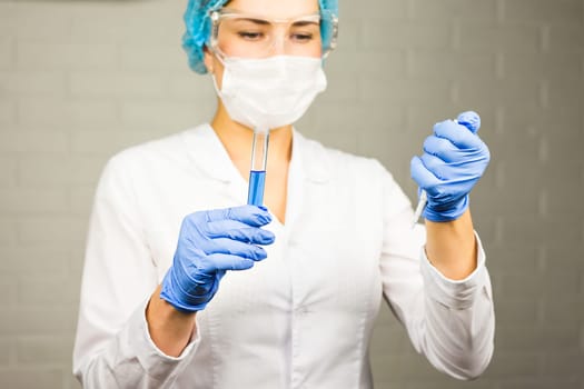 Close-up of glass tube with blue fluid in nurse hand during medical test.