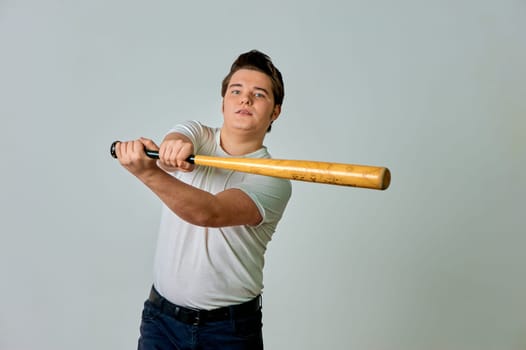 A man with a bat in his hands swings on a gray background. High quality photo