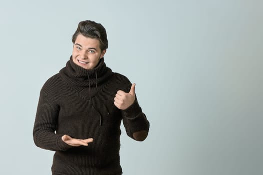 a man in a brown sweater and a bright color points to something and perfectly, showing an empty space with his thumb, shows everything on a light background, copy space. High quality photo
