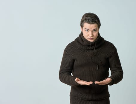 A man on a gray background in a brown sweater showing emotions, shows his hands. High quality photo