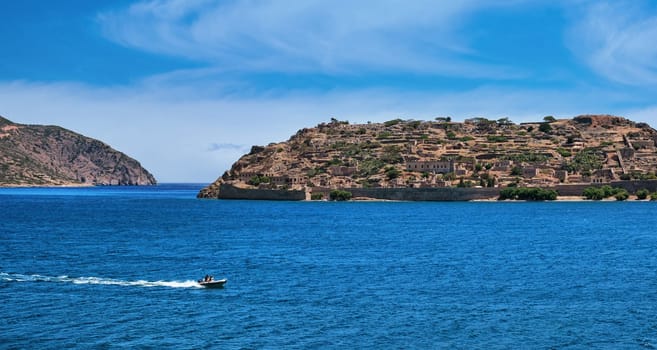 Beautiful view of west bank of Spinalonga island and Venetian fortress on clear sunny summer day on Crete, Greece. Boats passing, old fortifications, calm blue sea. film grain