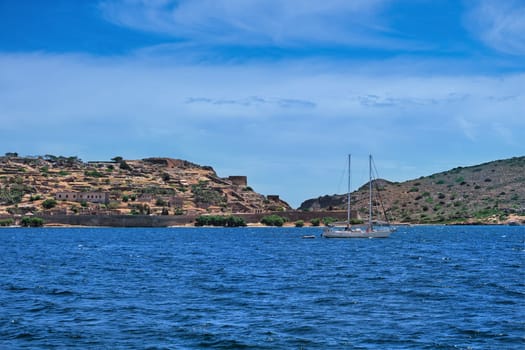 Typical seascape of Spinalonga island, Venetian fortress and floating anchored yacht in front of it on clear sunny summer day, Crete, Greece. film grain