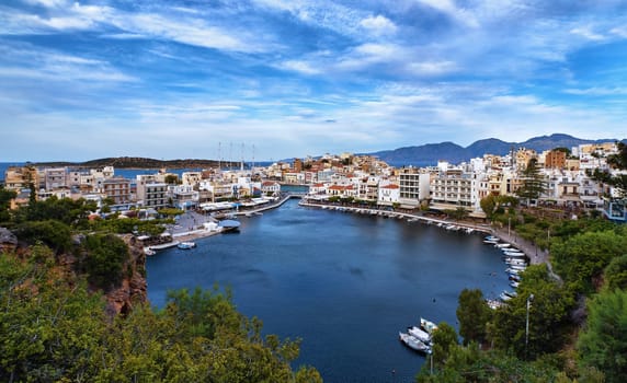 Colorful view of Voulismeni lake and Agios Nikolaos town on Crete island, Greece in evening. Boats, cafes, restaurants, ship, marina, promenade.