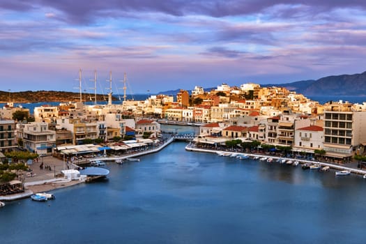 Colorful view of Voulismeni lake and Agios Nikolaos town on Crete island, Greece at sunset. Boats, cafes, restaurants, ship, marina, promenade.