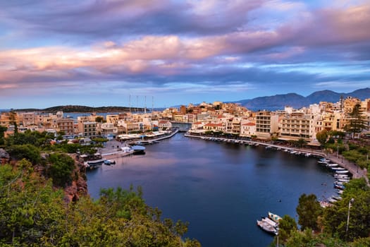 Colorful view of Voulismeni lake and Agios Nikolaos town on Crete island, Greece at summer sunset. Boats, cafes, restaurants, ship, marina, promenade.