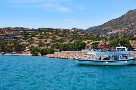 Classic view of beautiful harbor on Greek island of Crete, Greece with hills and houses in background, anchored ferry and calm blue sea on clear sunny summer day