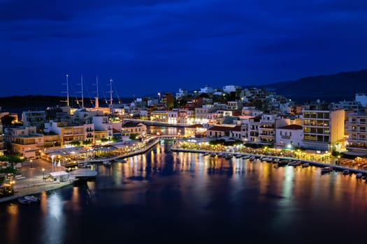 Colorful view of Voulismeni lake and Agios Nikolaos town on Crete island, Greece at dusk. Boats, cafes, restaurants, ship, marina, promenade.