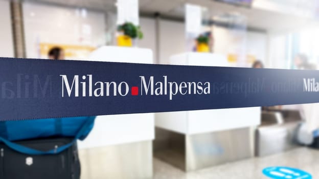 Malpensa, Italy, June 21 2023: Blue retractable belt barrier with white Milano Malpensa airport logo. Italian international airport located in the region of Lombardy. Illustrative editorial