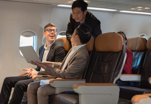 Businessman passengers having discussion, working together on laptop in airplane cabin. Business work and travel concept