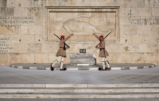 Ceremony of Presidential guard Evzones by the Greek tomb of Unknown Soldier. Evzones in summer uniform face each other, legs in stepping position, hands up. Close shot.