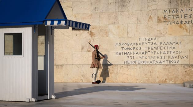 Evzone stand still on guard, by the wall of the tomb of Unknown soldier next to guard box in afternoon.