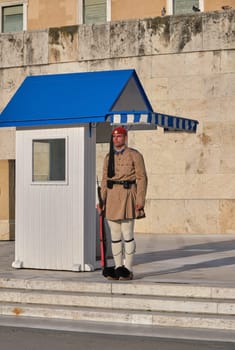 Evzone in summer uniform stand still in shade of guard box in afternoon.