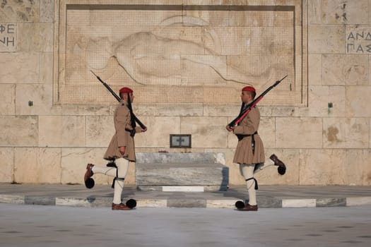 Ceremony of Presidential guard Evzones by the Greek tomb of Unknown Soldier. Evzones in summer uniform face each other, knees bent . Close-up shot.