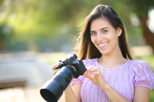 Happy photographer checking camera looking at you in a park