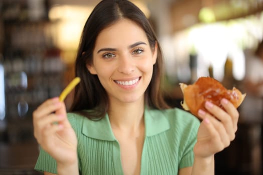 Happy restaurant customer holding potato and sandwich looking at you