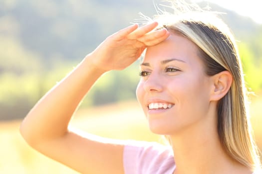 Happy woman with hand on forehead protects from sun in nature