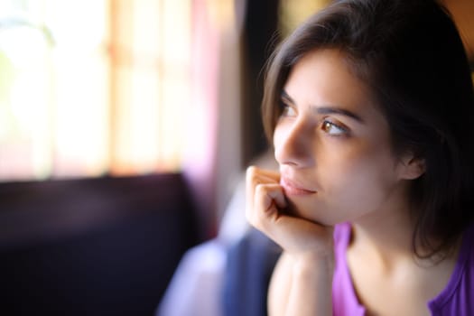 Pensive woman relaxing looking through a window sitting at home
