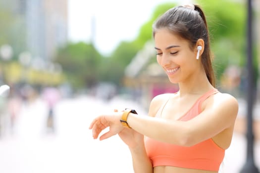 Happy runner wearing earbud selecting music on smartwatch before run in the street