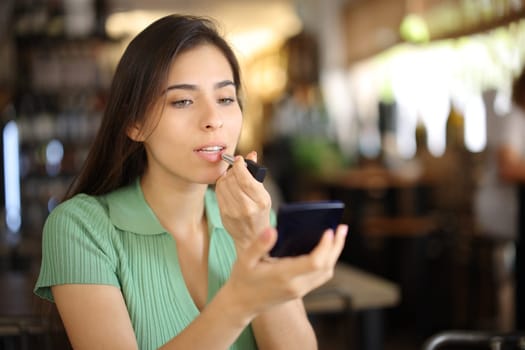 Woman painting lips before dating in a restaurant interior