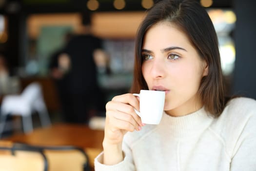 Serious woman drinking coffee alone in a bar looking away