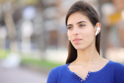 Serious woman wearing earbud listening audio standing in the street