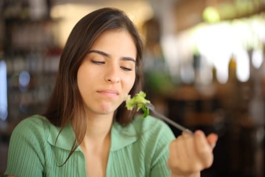Disgusted woman eating lettuce sitting in a restaurant