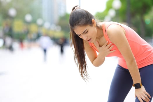 Exhausted runner touching chest breathing in the street