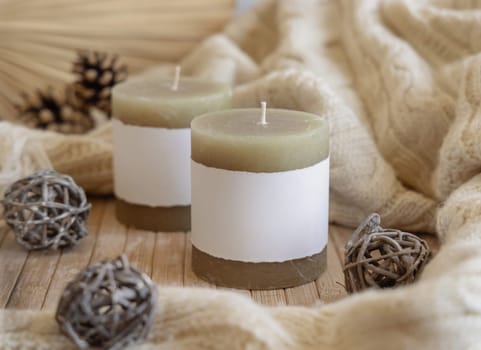 Candles with blank paper label near natural wooden decorations and knitted sweater, Close up, copy space. Boho packaging mock up. Home decorations, Bohemian or scandinavian style