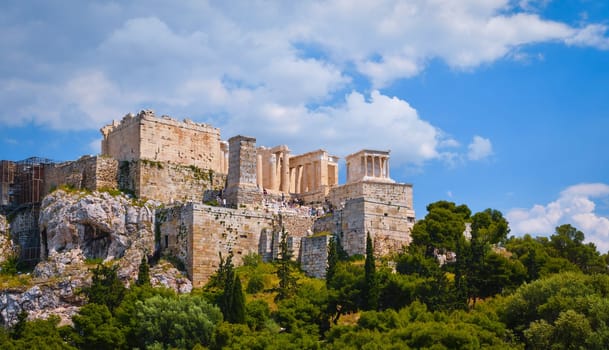 View of Acropolis hill from Areopagus hill in summer daylight with great clouds in blue sky, Athens, Greece. UNESCO world heritage. Propylaea entrance, Agrippa's monument, Parthenon. Fresh green foliage. in foreground, great clouds in blue sky