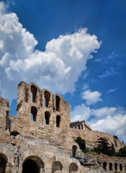 Diagonal dynamic composition of Odeon of Herodes Atticus theater arches on Acropolis hill, Athens, Greece, against bright blue sky and super clouds. Ancient ruins still used as venue for concerts and festivals. UNESCO world heritage. Vertical shot.