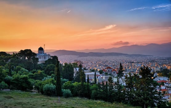 Beautiful and colorful view of Athens, Greece and its residential areas from Pnyx hilltop in soft evening sunlight and great sunset sky. National observatory of Athens in foreground.