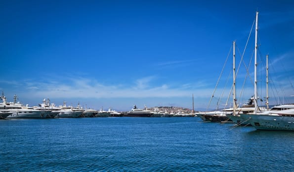 Boats and yachts anchored or moored in a marina and by its promenade on a bright summer day. Concept of seascape, voyage, sea adventure, private yachting weekend, summer vacations.