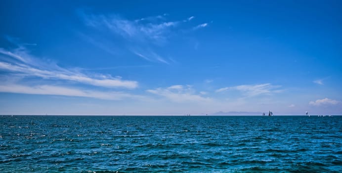 Panoramic beautiful seascape on a bright summer day with few sailing boats afar, great sky with dynamic clouds. Peaceful vacation, meditative, relaxing view. Weekend by sea, beach, contemplation.