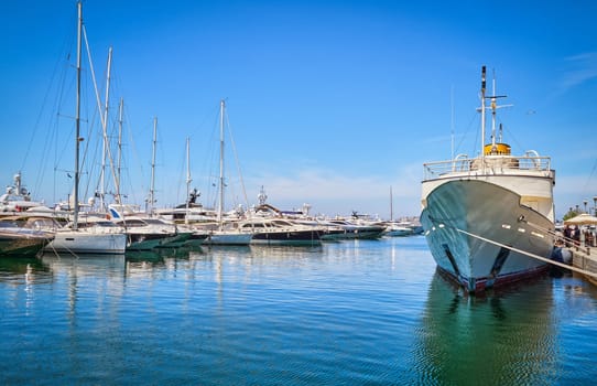 Boats and yachts anchored or moored in Athens marina and by its promenade in Glyfada on a bright summer day. Concept of seascape, voyage, sea adventure, private yachting weekend, summer vacations. Athens, Greece