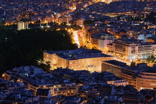 Night view Hellenic Parliament in Syntagma square brightly lit up and ruins of temple of Olympian Zeus behind it shot from hill of Lycabettus, Beautiful iconic image of center of Athens, Greece.
