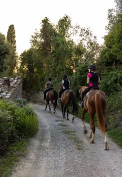 Montemassi, Italy - September 13, 2022: A woman and two girls during a horseback ride on a gravel road in Montemassi, Italy