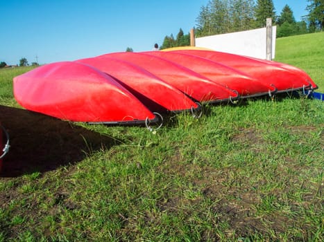 Red canoes in a row upside down on a hilly meadow in Bavaria.