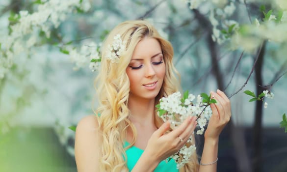 Beautiful young woman with blonde long hair in spring blooming garden on a sunny day against flowers trees background