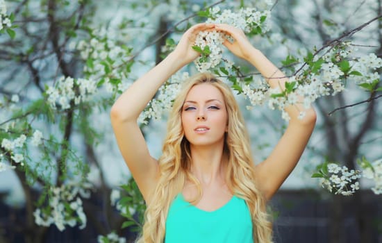 Beautiful young woman with blonde long hair in spring blooming garden on a sunny day against flowers trees background