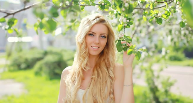 Beautiful young woman with blonde long hair in spring blooming garden on a sunny day against flowers trees background