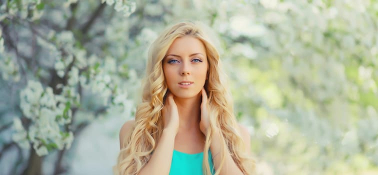 Beautiful young woman with blonde long hair in spring blooming garden on a sunny day against flowers trees background