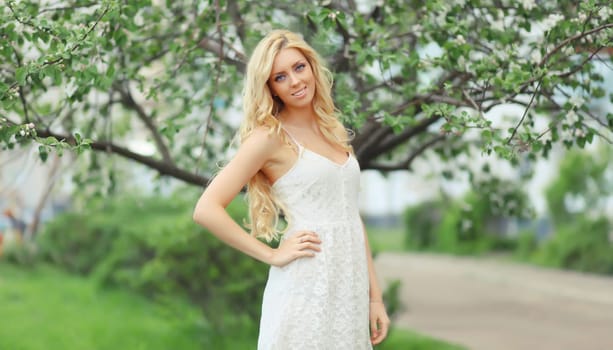 Beautiful young woman with blonde long hair in spring blooming garden on a sunny day against flowers trees background