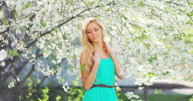 Beautiful young woman with blonde long hair in spring blooming garden on a sunny day against flowers trees background