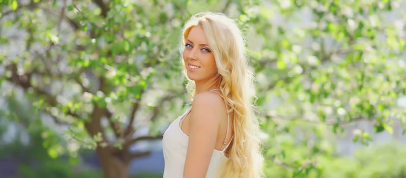 Beautiful young woman with blonde long hair in spring blooming garden on a sunny day against flowers trees background